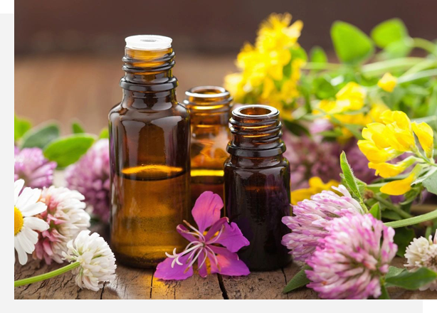 Three bottles of essential oils and flowers on a table.